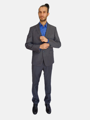 A male model wearing a gray suit, blue shirt, and dark shoes standing against a white background.